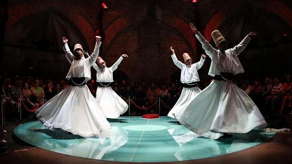 The dancers, dressed in flowing white robes, spin in repetitive circles while their arms are gracefully extended.