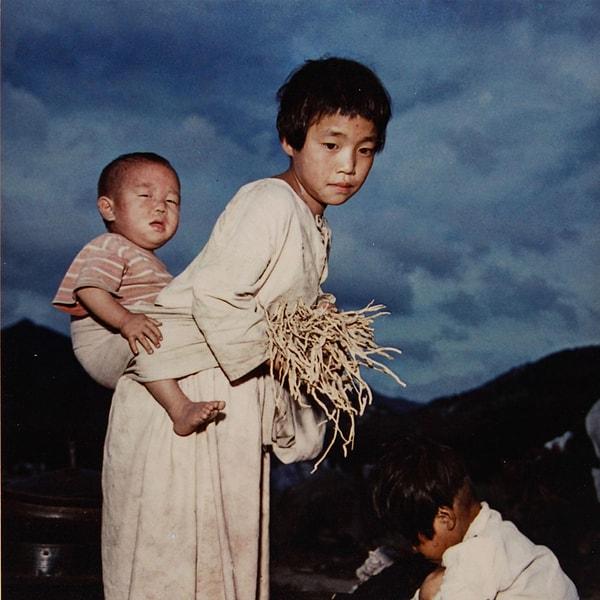 7. Kore Savaşı sırasında Seul'deki bir mülteci kampında küçük kardeşini sırtında taşıyan bir kız çocuğu. (Ağustos 1951)