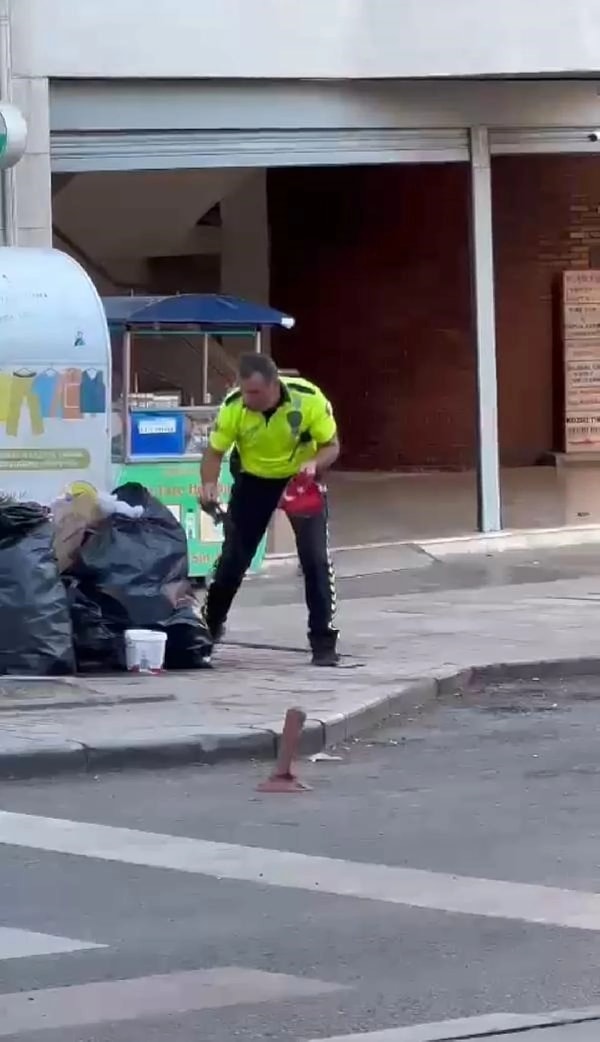 Polis memuru, çöp poşetiyle atılan Türk bayrağını elleriyle temizledikten sonra polis aracına koydu.