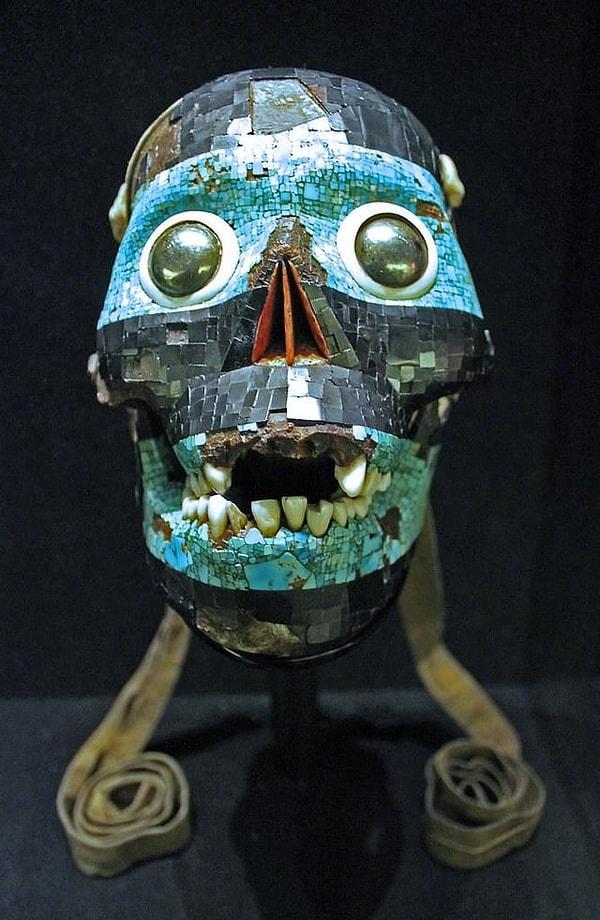 15. Tanrı Tezcatlipoca'nın maskesi, turkuaz ve linyit mozaik ile kaplanmış bir insan kafatasından yapılmıştır. Kabuklu deniz kabuğu arkasında demir pirit gözleri bulundurmaktadır. Burun boşluğu kırmızı spondilus kabuğuyla kaplıdır. (M.S 15. yüzyıl)