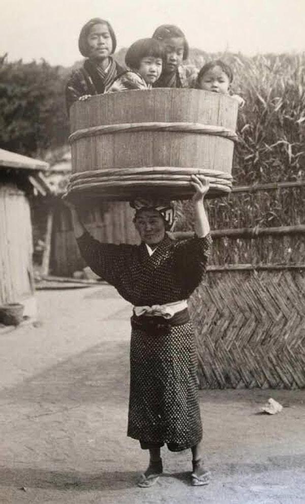 12. Çocuklarını başının üstünde kovayla taşıyan Japon kadın. (Japonya, 1900'ler)