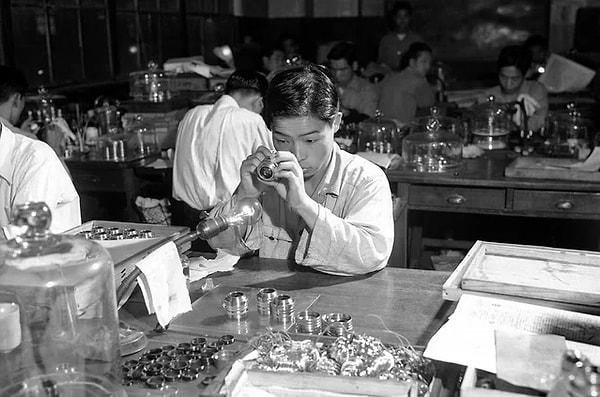9. Tokyo'daki Nikon fabrikasında bir fotoğraf makinesi merceğini inceleyen bir işçi. (Japonya, 1952)